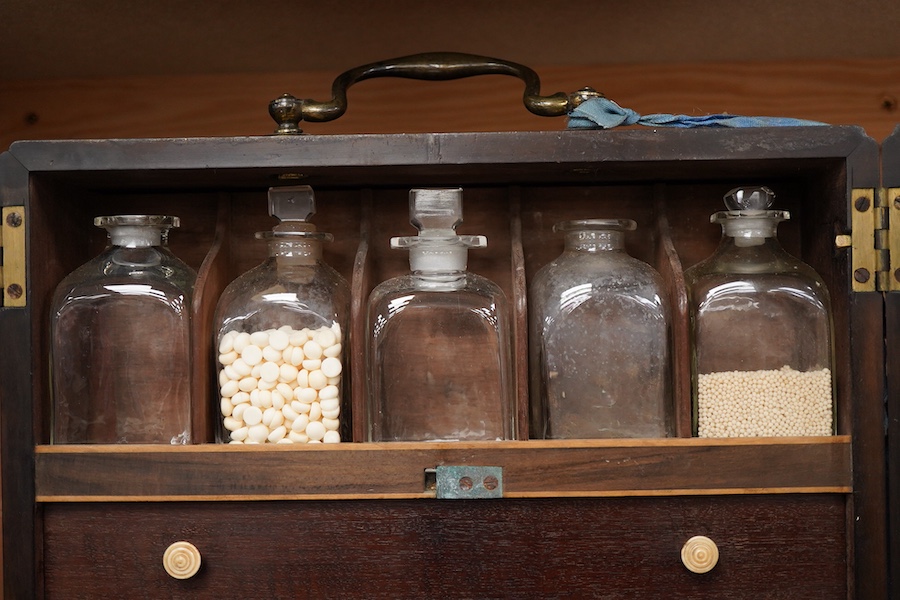 A 19th century mahogany apothecary cabinet, interior with fitting compartments containing twenty-one glass bottles, most with stoppers, five drawers with ivory knobs containing a miniature pestle and water, mixing glasse